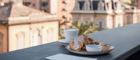 A table with a croissant, a cup of coffee, and a plate with a pastry, overlooking a cityscape with buildings and mountains.