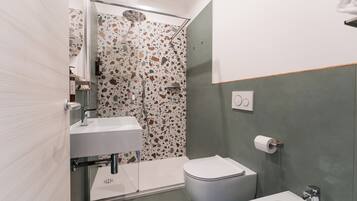 A modern bathroom with a white sink, a toilet, and a bidet. The walls have a terrazzo finish with multicolored stone patterns.