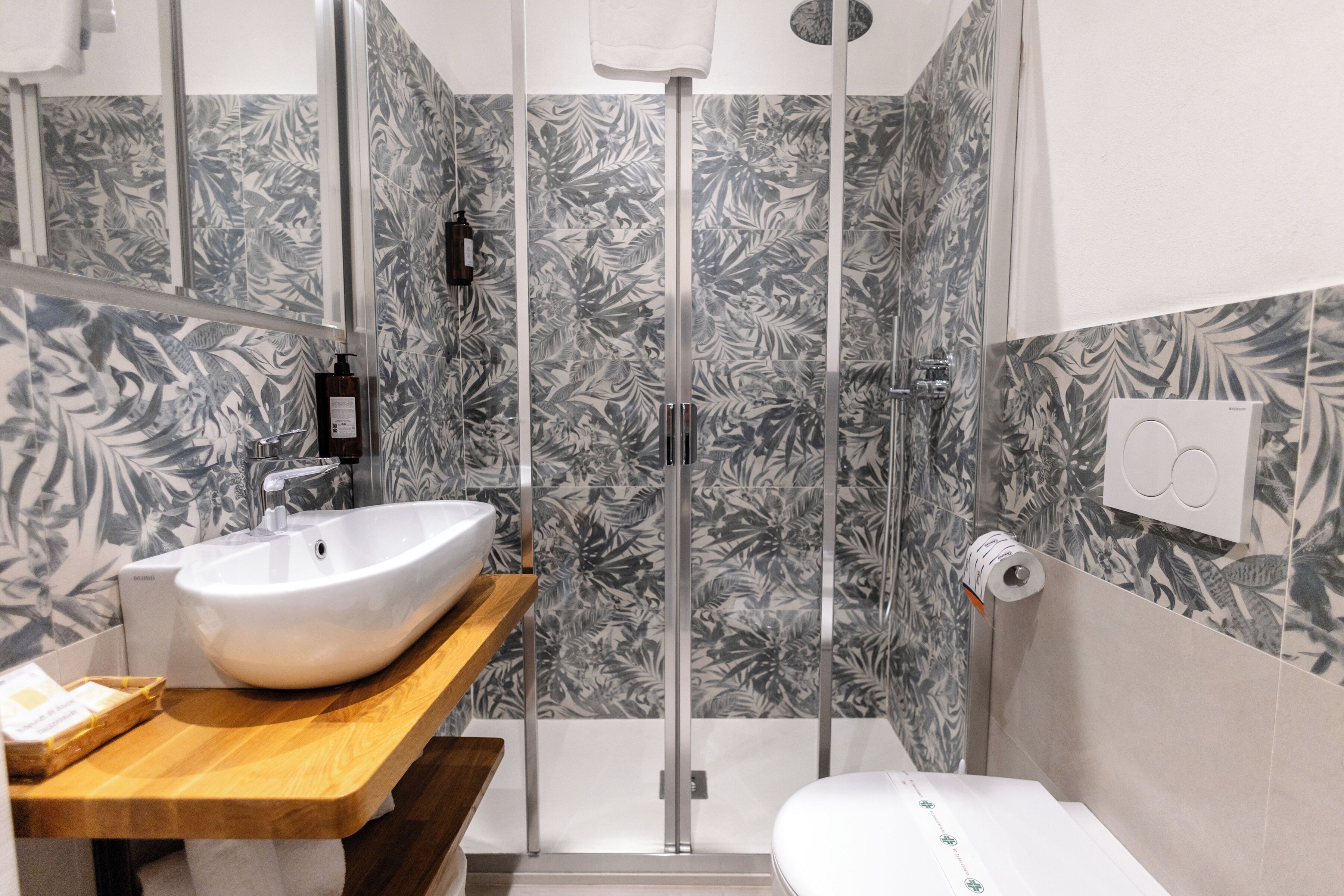 A modern bathroom with a wooden vanity, a white sink, a glass shower enclosure, and patterned wall tiles.