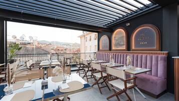 Un restaurant situé sur le toit, avec des tables et des chaises, offrant une vue sur la ville, et une horloge indiquant l’année 2024.