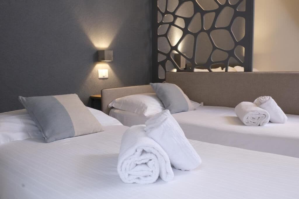 Une chambre d’hôtel avec deux lits, chacun étant équipé de draps et d’oreillers blancs. Des serviettes sont soigneusement pliées sur les lits.