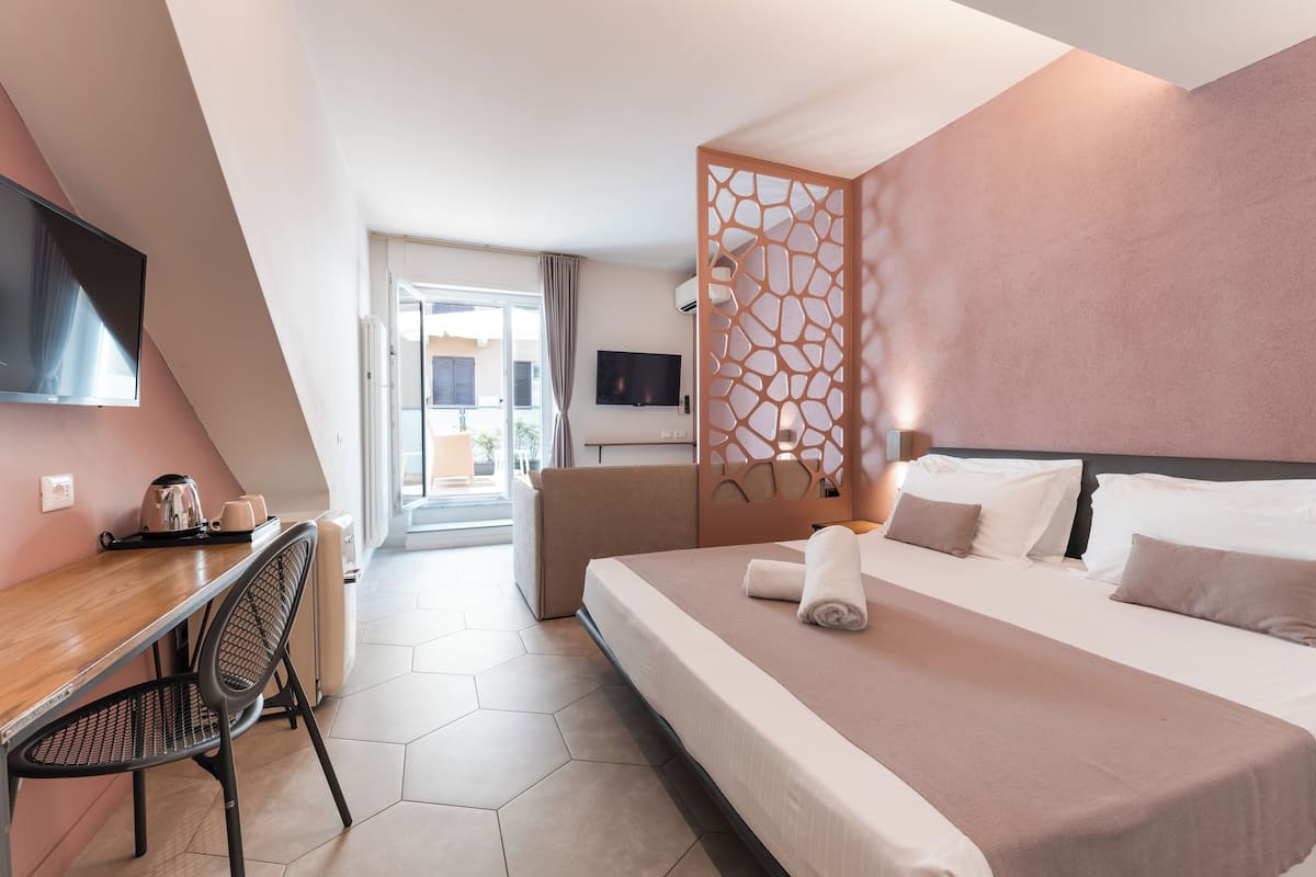 Habitación de hotel con cama, escritorio, silla, televisor y vista al exterior.