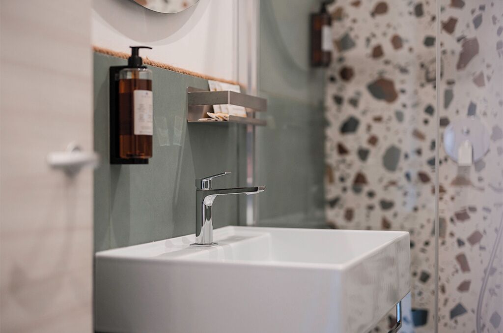 A bathroom with a white sink, a modern faucet, a soap dispenser, and a towel rack.