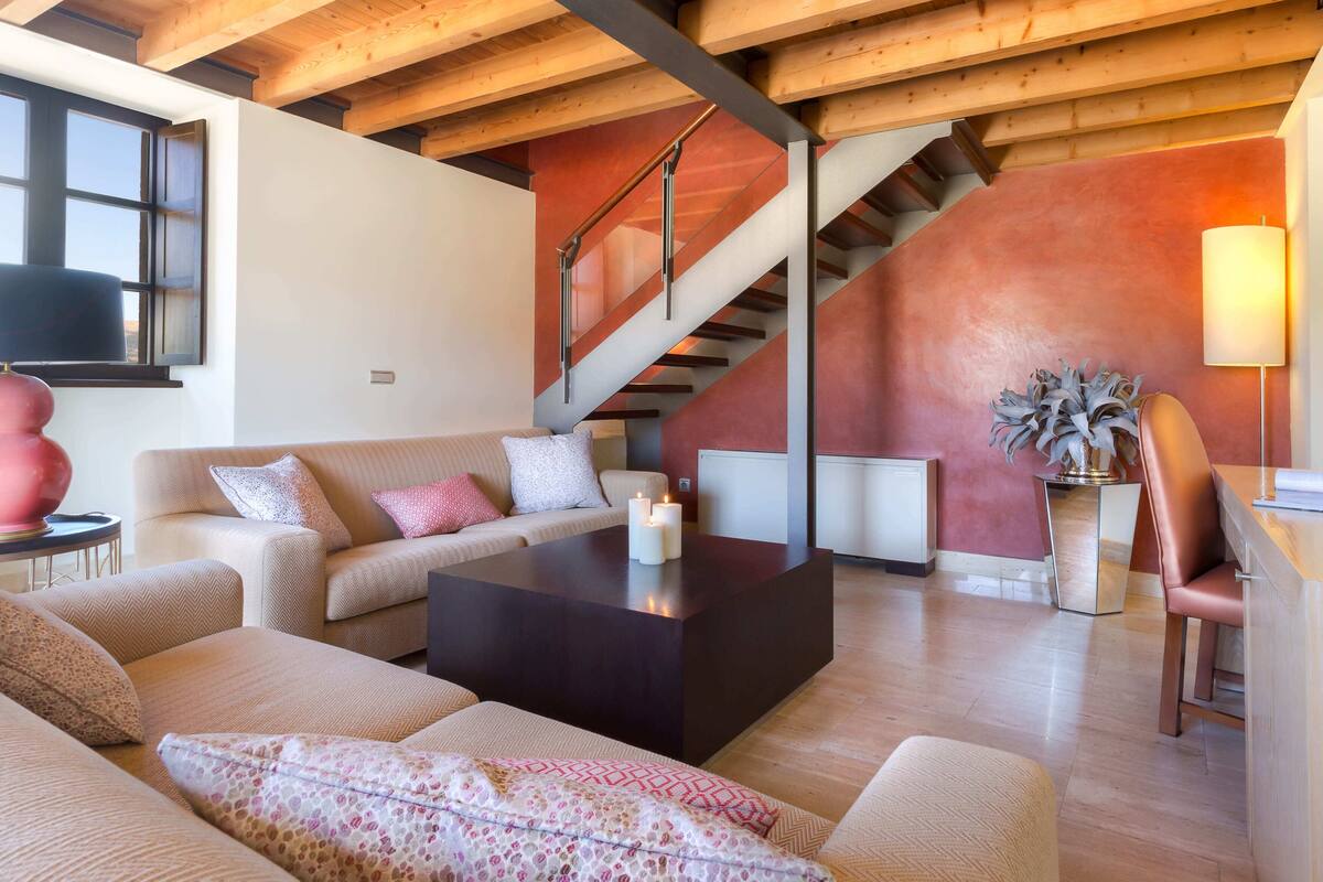 Una sala de estar moderna con un conjunto de sofás, una mesa de centro y una escalera con pared roja.