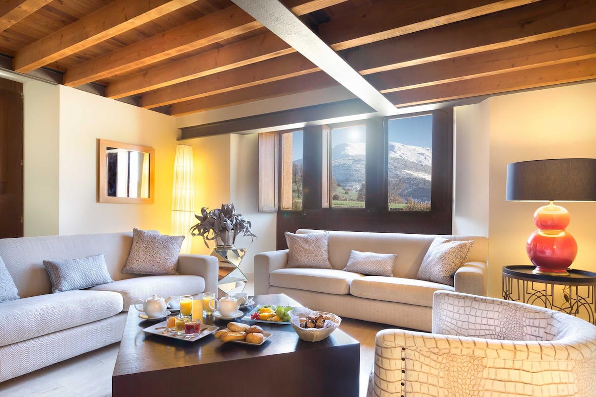 Una sala de estar acogedora con dos sofás, una mesa de centro con alimentos para el desayuno, y vistas a las montañas a través de amplias ventanas.
