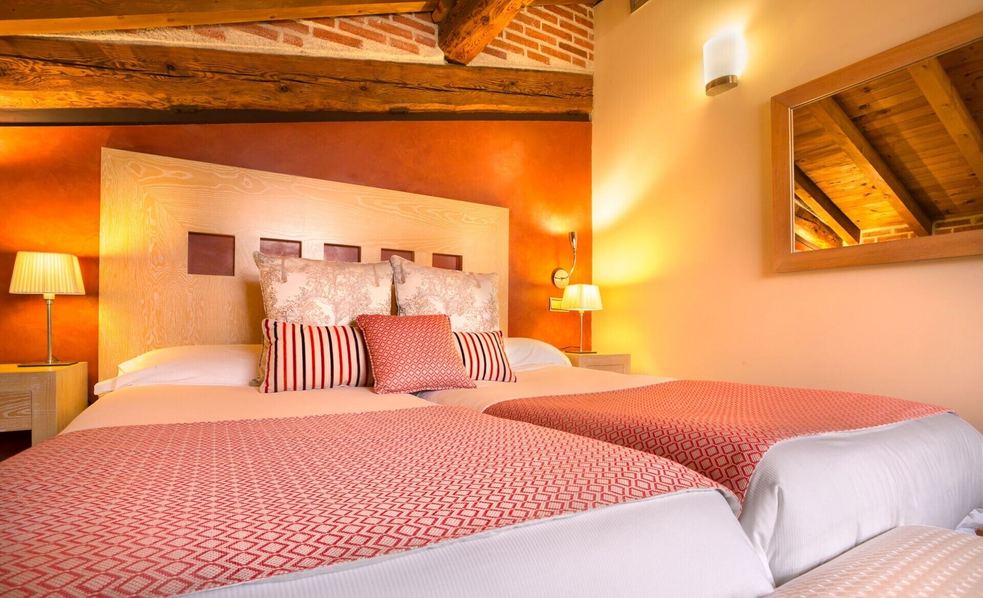 A hotel room with two beds, wooden beams on the ceiling, and a large mirror on the wall.