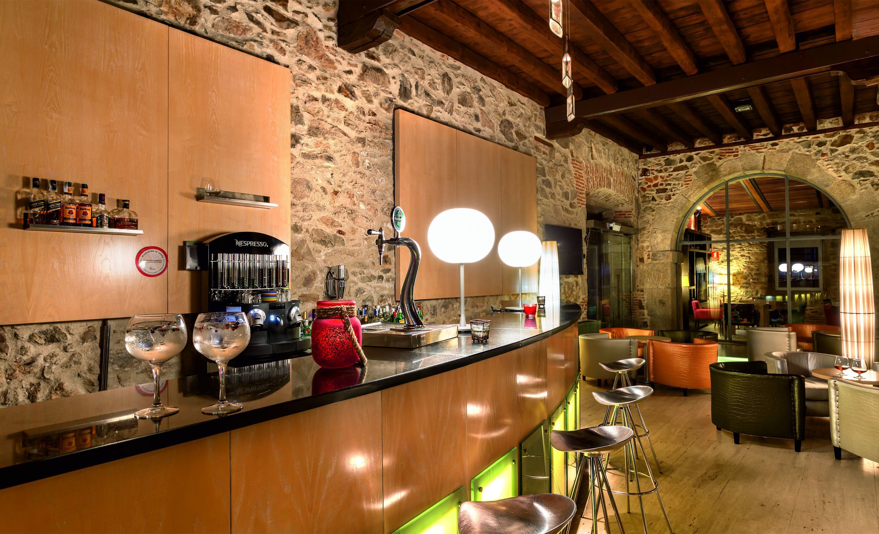 Zona de bar con pared de piedra, mostrador de madera y taburetes.