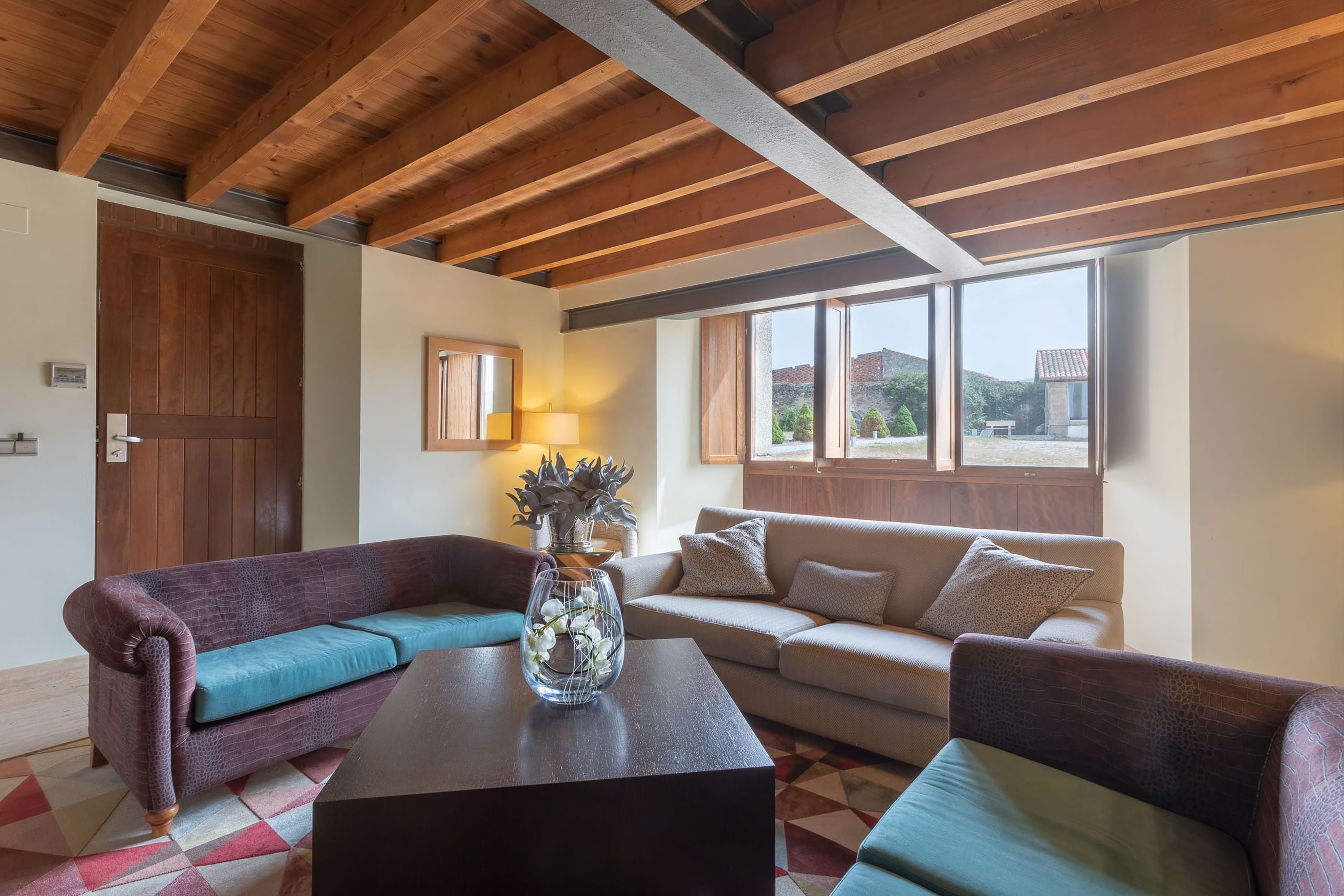 Una sala de estar con techo de madera, un ventanal grande, un sofá, una mesa de centro y una puerta.