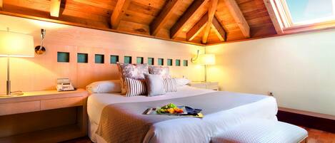 Un dormitorio con techo de madera, una cama con múltiples almohadas, mesitas de noche con lámparas y una ventana.
