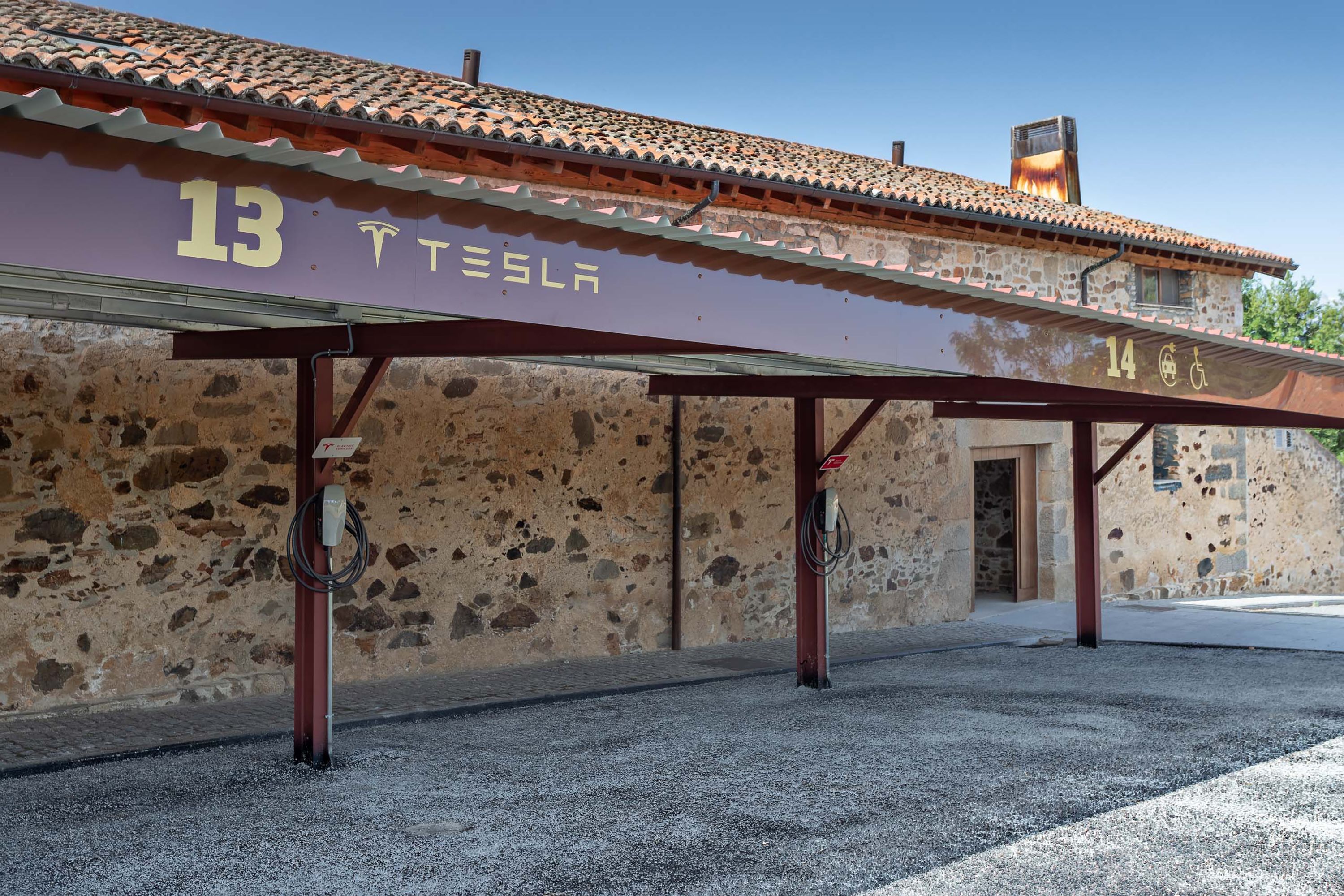 A building with a stone facade and a roof with terracotta tiles. There are two signs with numbers 13 and 14, and a wheelchair accessibility symbol.