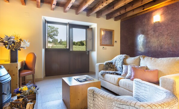 Un salón acogedor con techo de madera, un sofá con cojines estampados, una mesa de centro de madera y un jarrón con flores.
