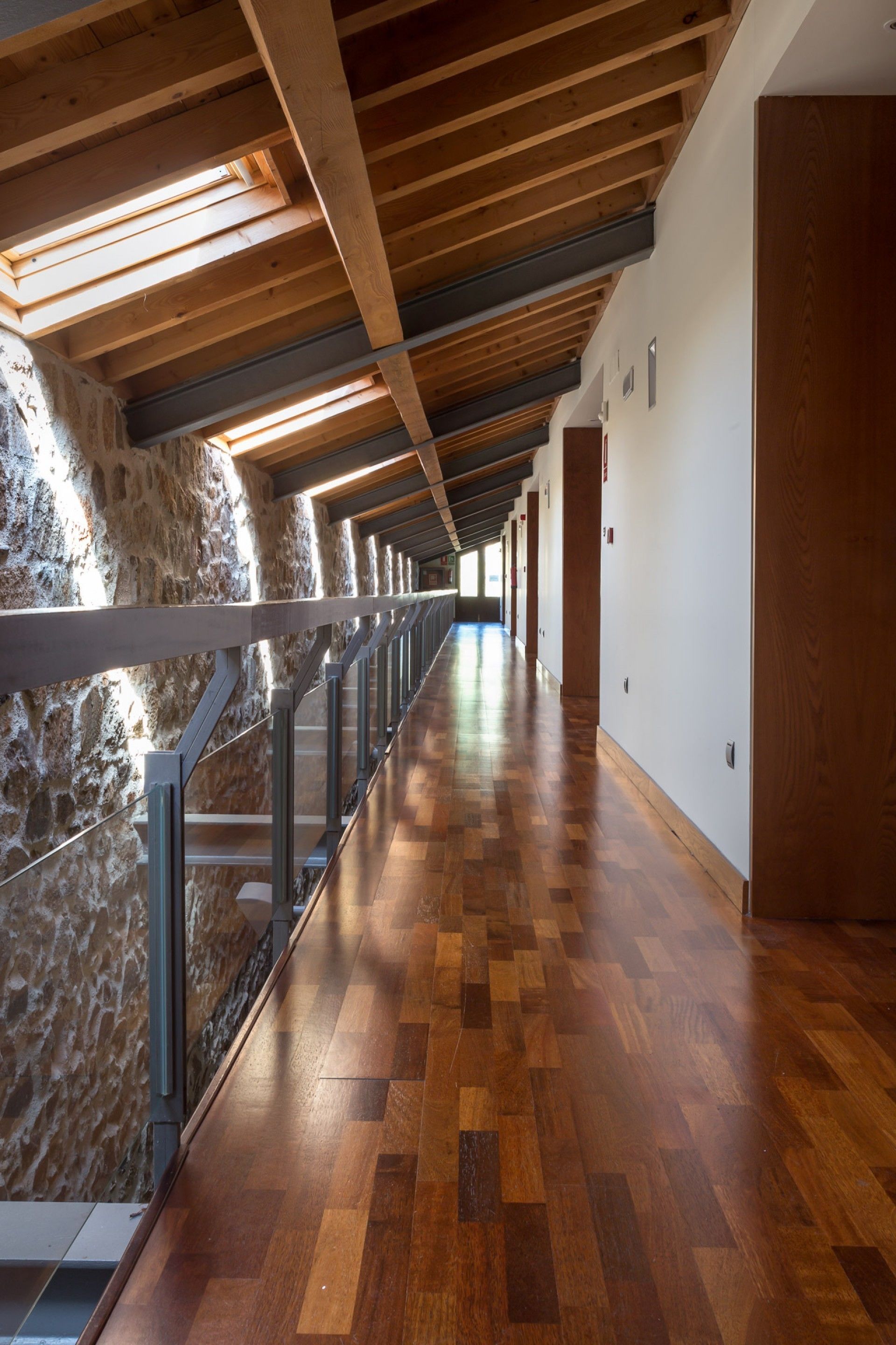 A long corridor with wooden flooring and a stone wall on one side.