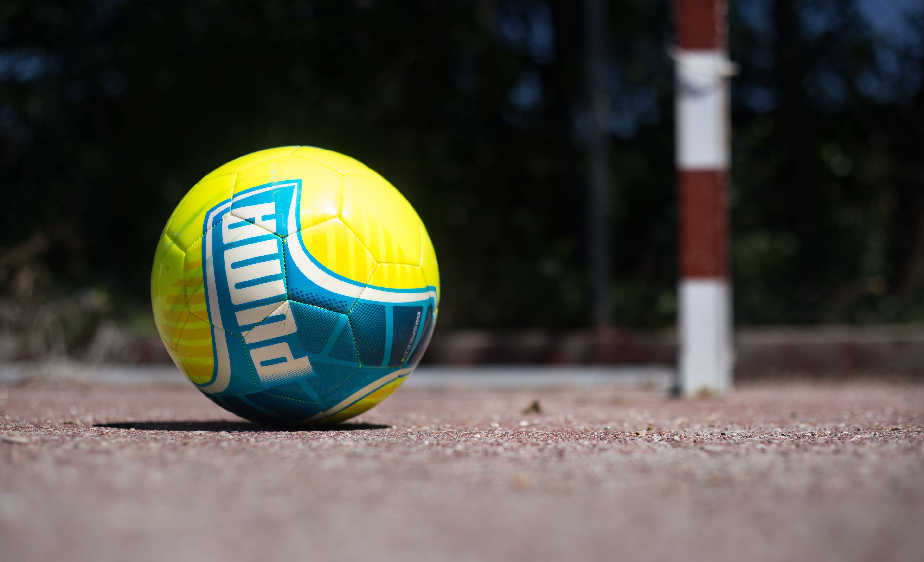 A yellow and blue sports ball with the word "PUMA" on it, placed on a sandy surface.
