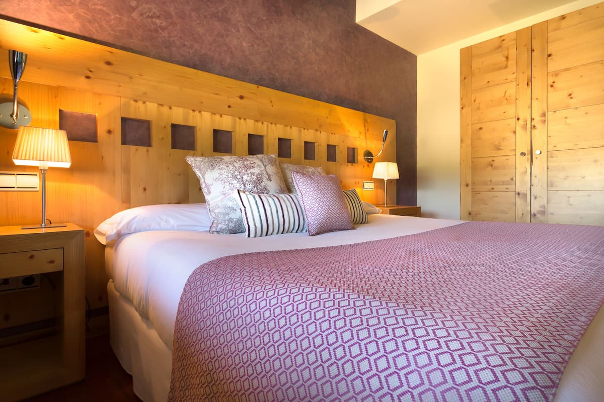 Un dormitorio con cabecera de madera, una cama grande con ropa de cama estampada, dos lámparas de noche y un armario de madera.