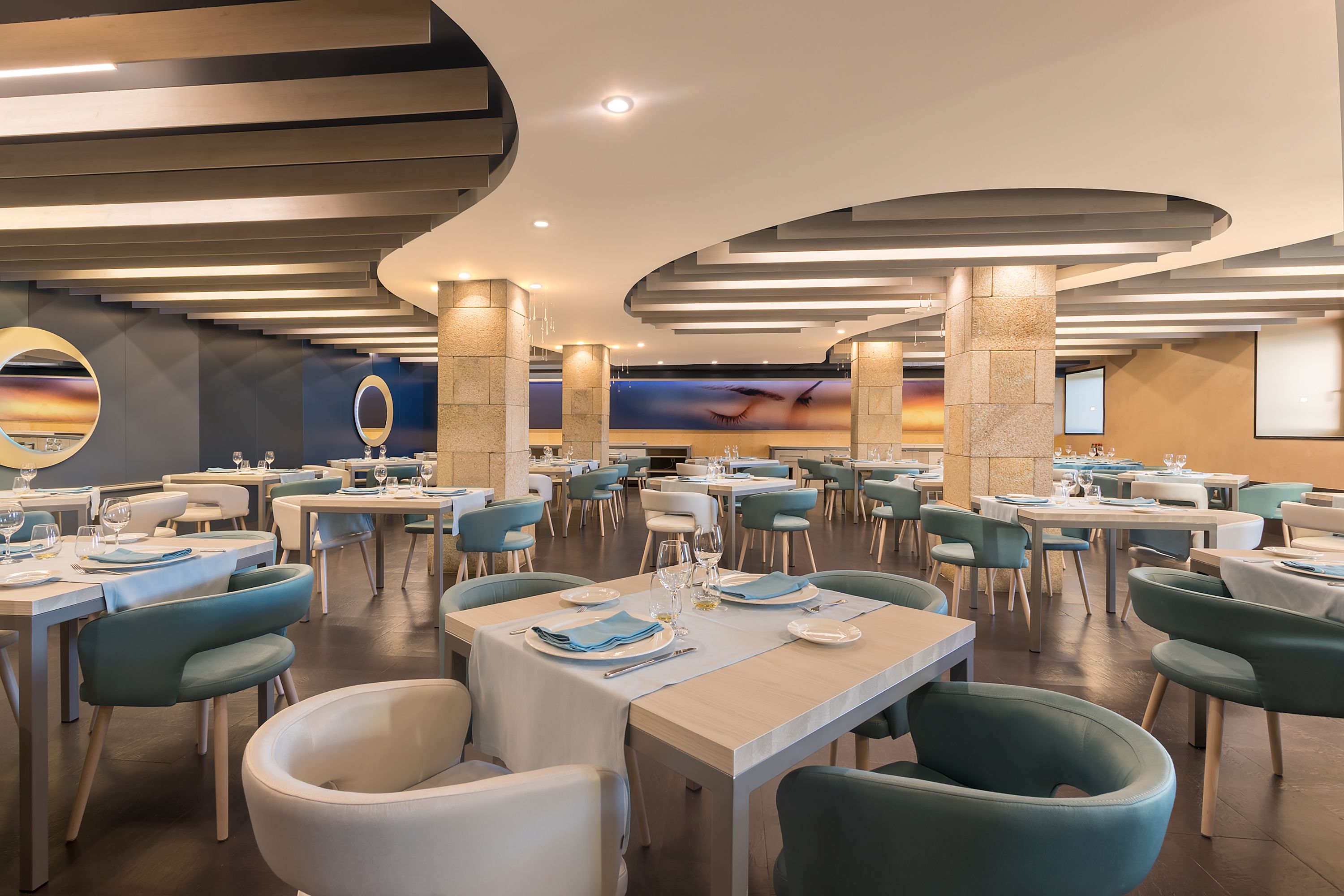 A spacious dining area with multiple tables and chairs, well-lit with recessed ceiling lights, and a large wall mural.