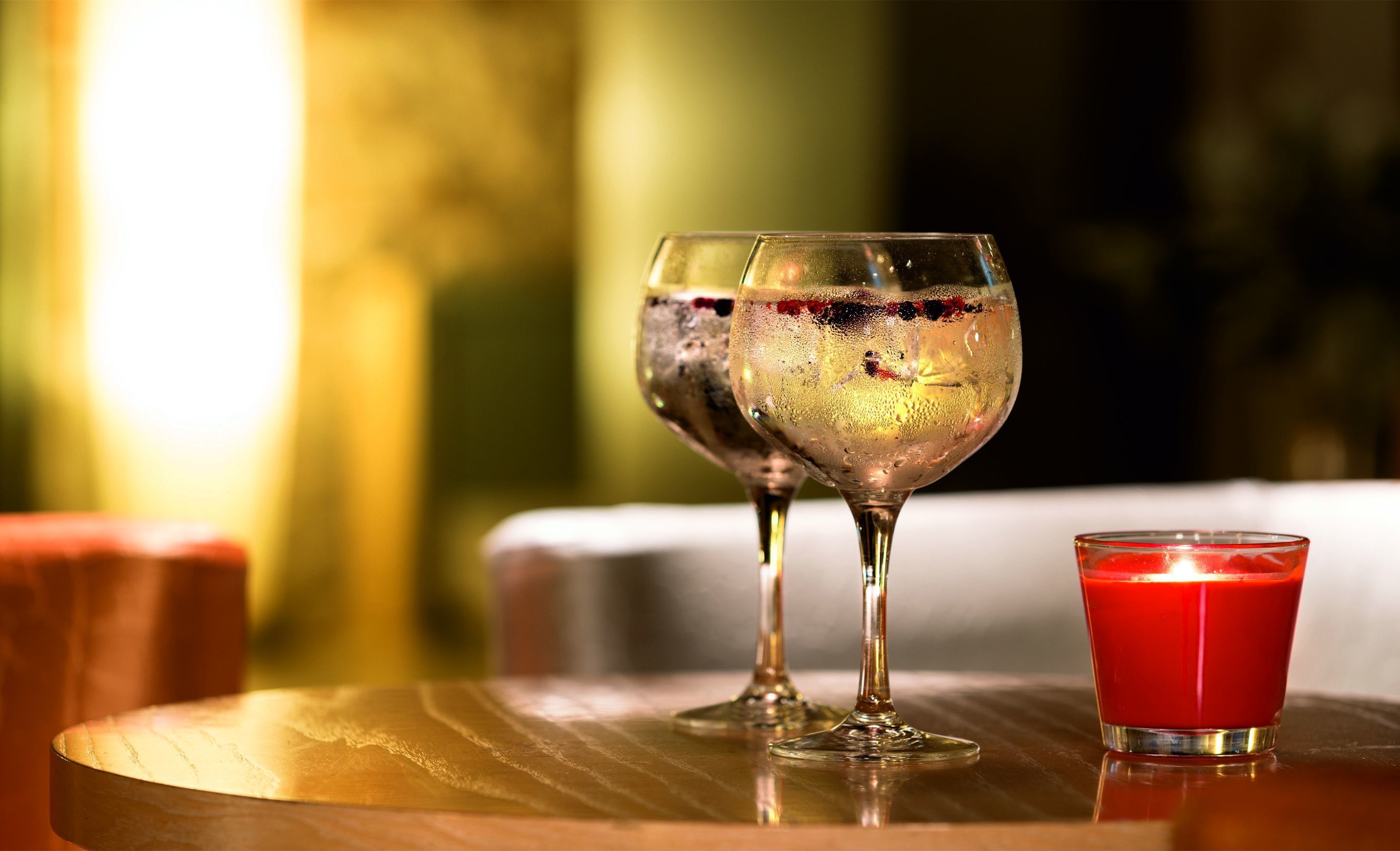 Dos copas de vino sobre una mesa de madera, con una vela roja a un lado.