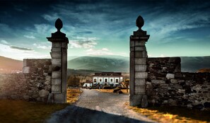 A stone gate leading to a building with a traditional architectural style, surrounded by a mountainous landscape.