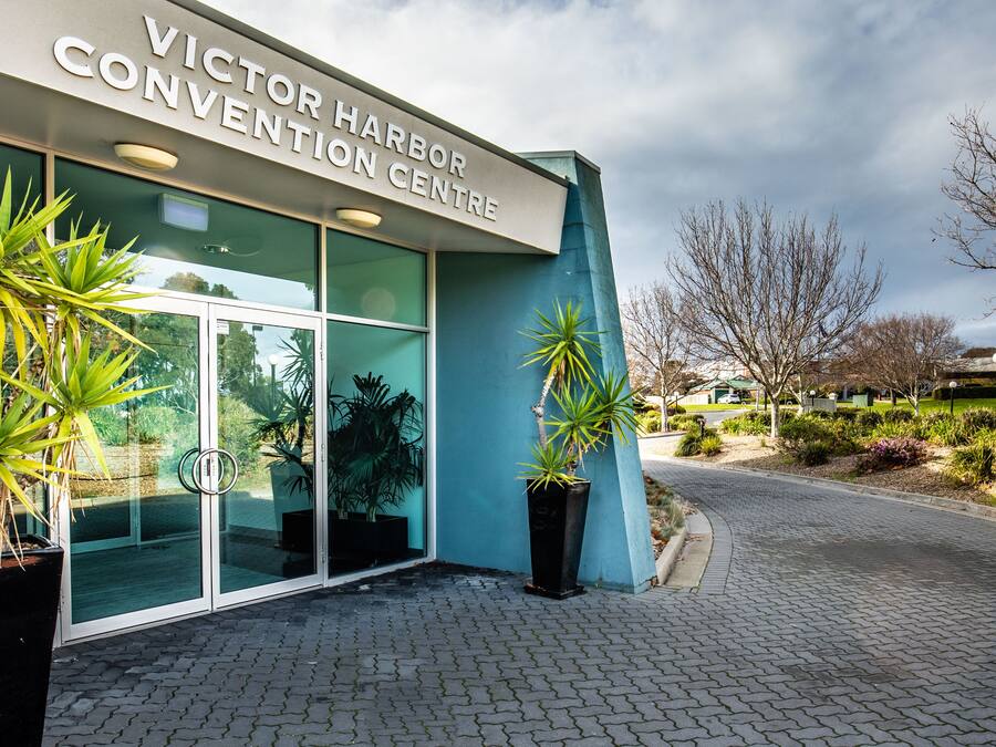 The exterior of the Victor Harbor Convention Centre with large glass doors, potted plants, and a paved entrance area.