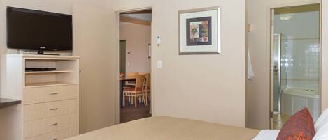Habitación de hotel con cama, televisor en un pedestal, un cuadro en la pared y baño visible a través de una puerta abierta.