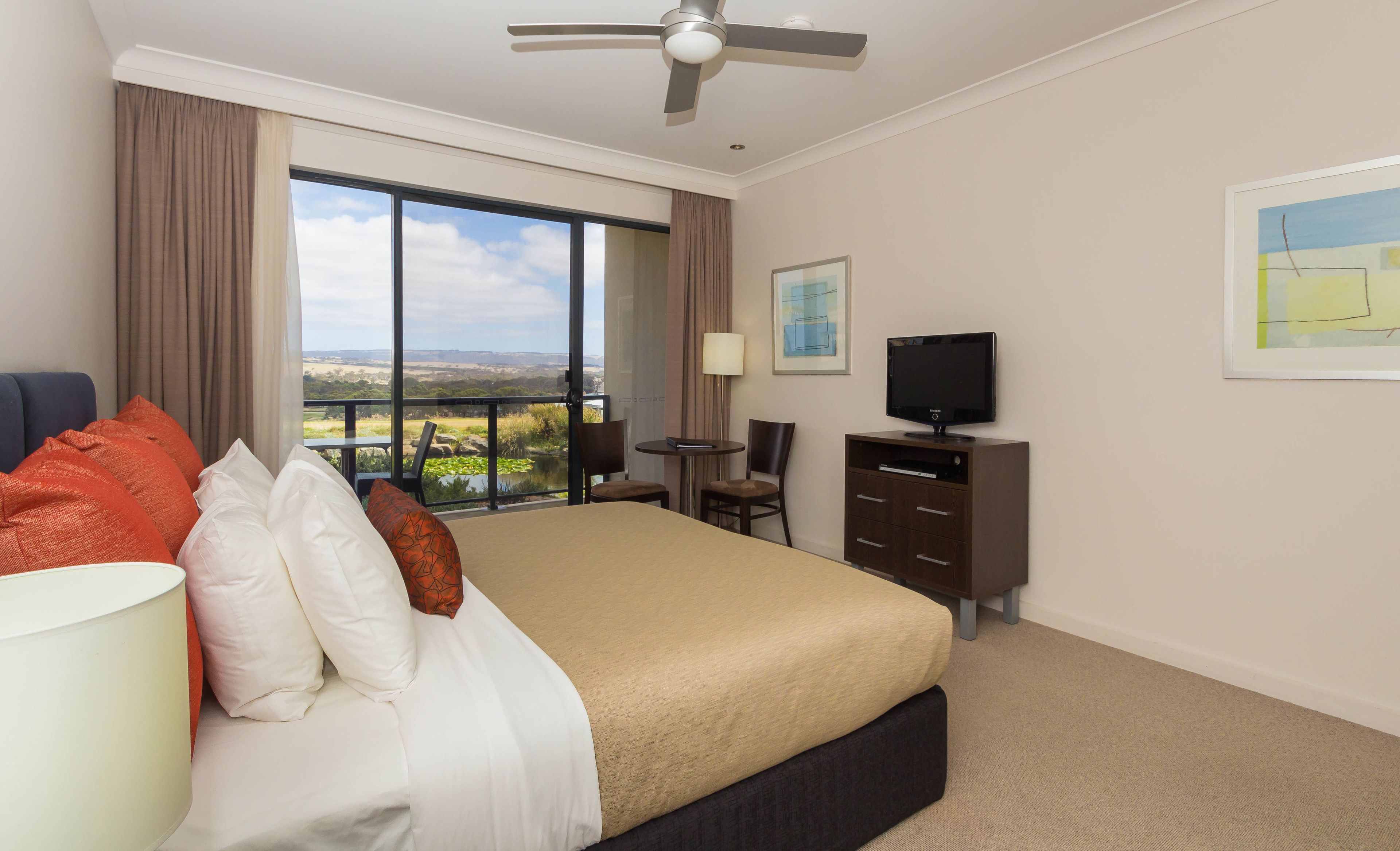A hotel room with a bed, a desk, a chair, a television, and a view of the landscape.