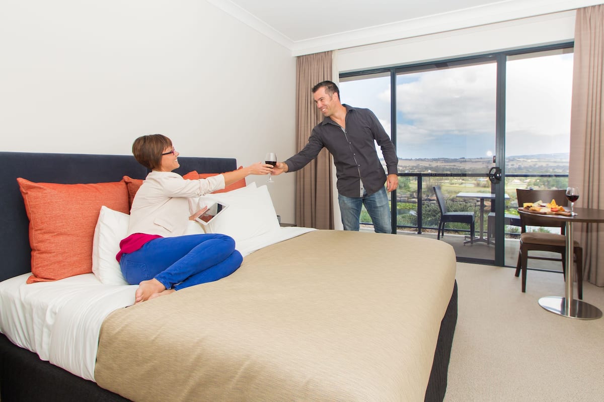 A hotel room with a bed, a balcony with a table and chairs, and a view of the landscape.