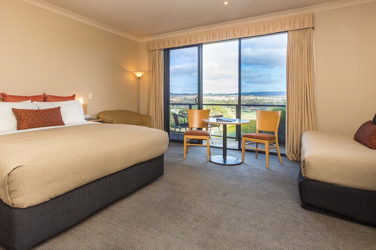 A hotel room with a large bed, two chairs, a small table, and a balcony with a view.