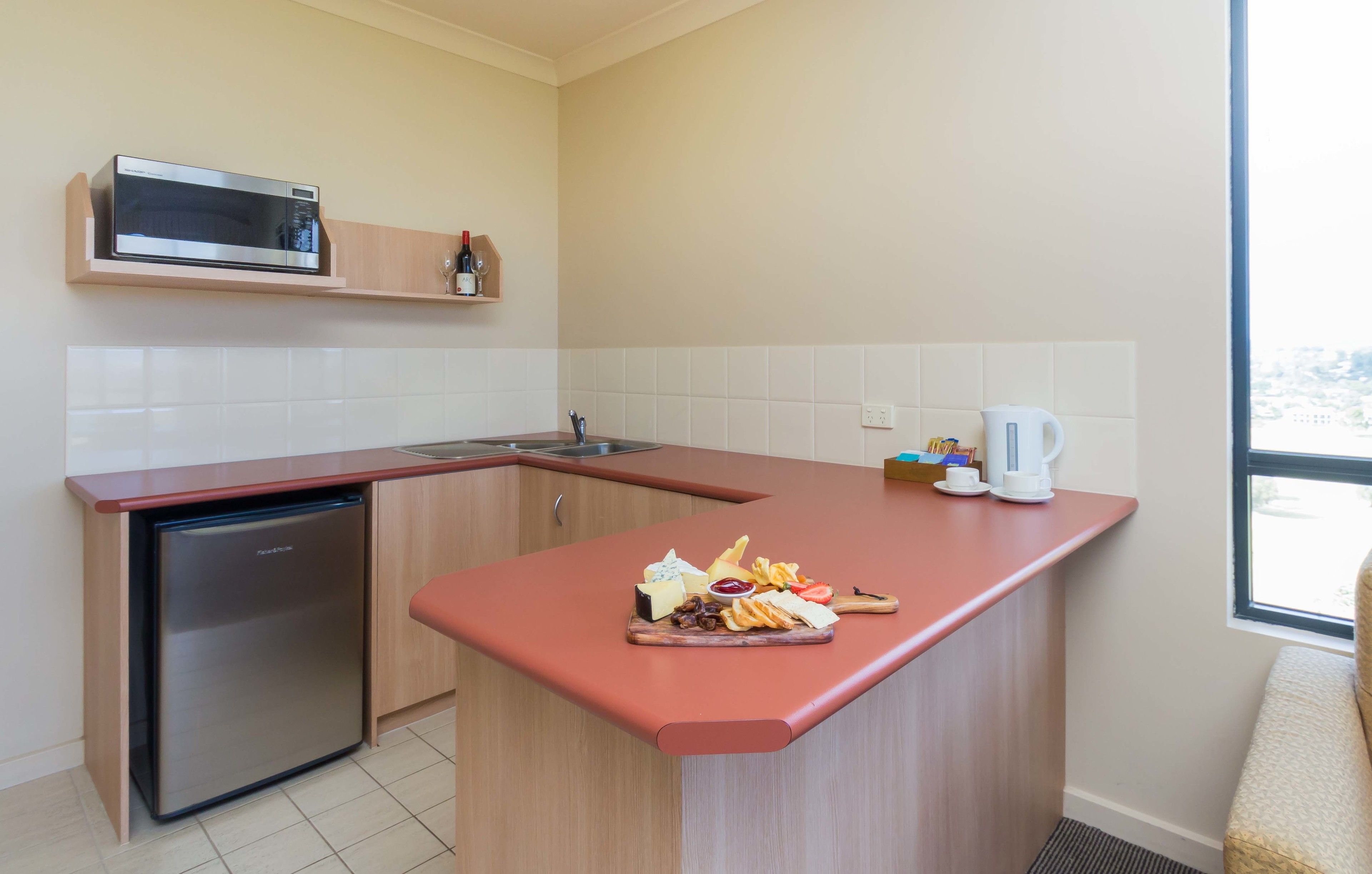 A compact kitchen with a microwave, sink, and a small refrigerator. A breakfast tray with eggs, cheese, and fruit is on the counter.