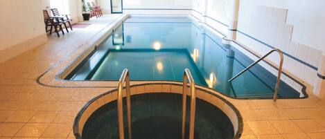 A swimming pool with a circular hot tub in the center, surrounded by chairs and a tiled floor.