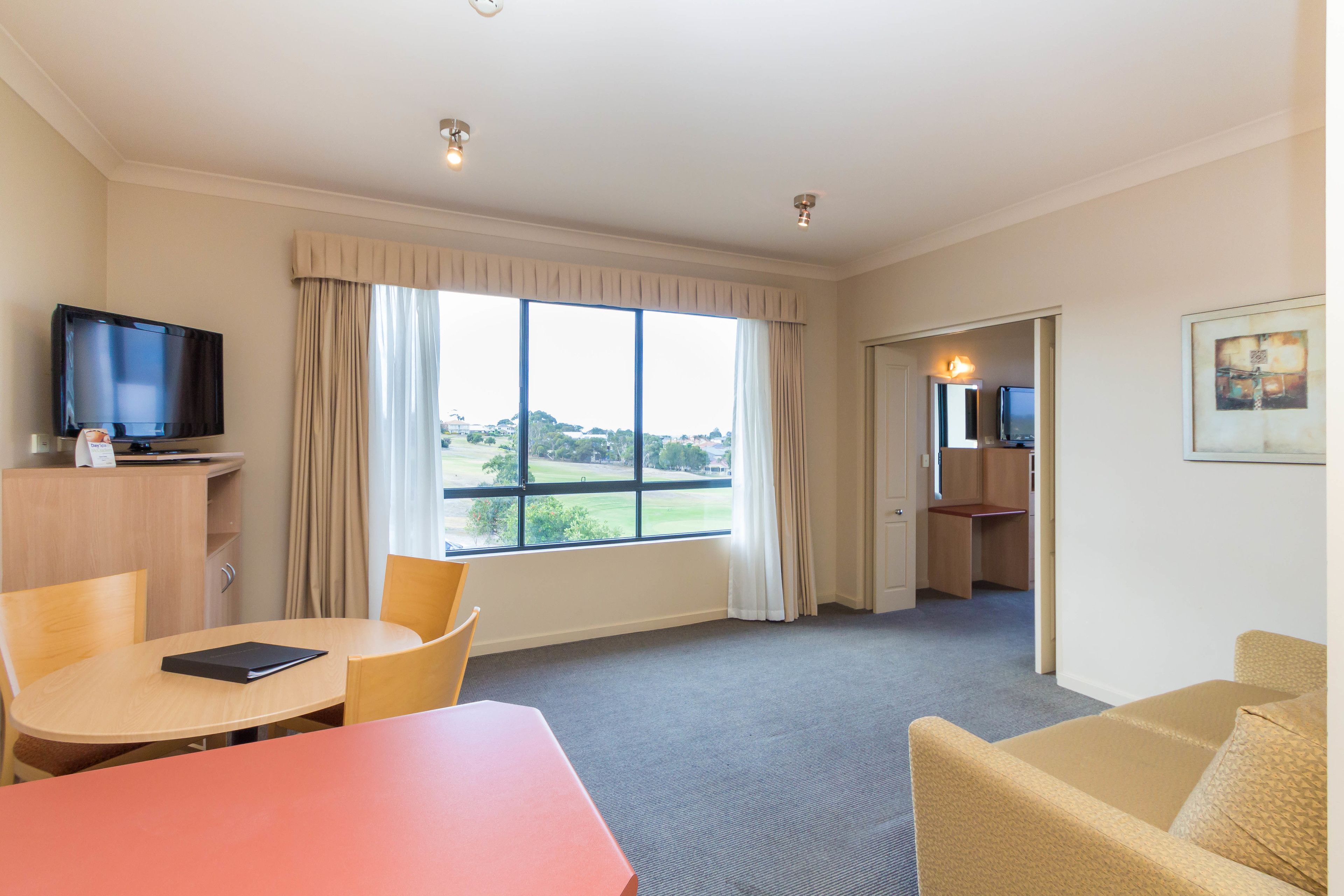 Quarto de hotel com uma grande janela, televisão, escrivaninha e sofá.