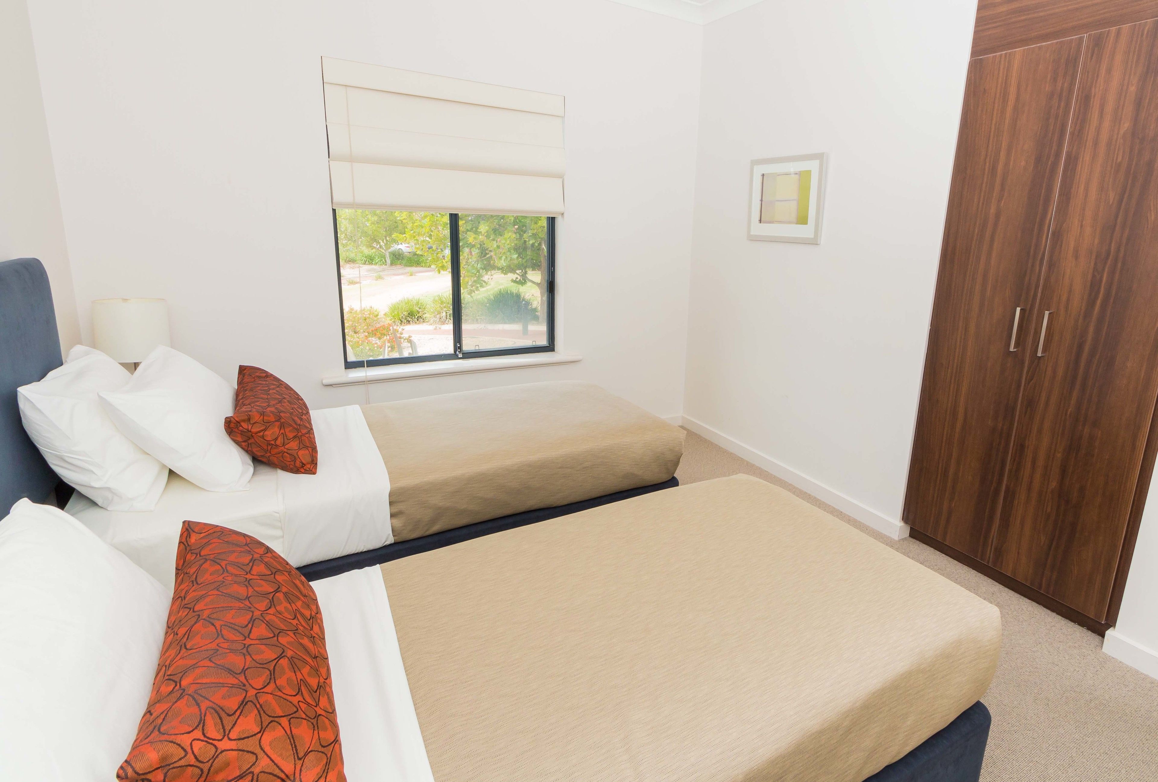 A bedroom with two beds, a window with a view, a wardrobe, and a bedside table.