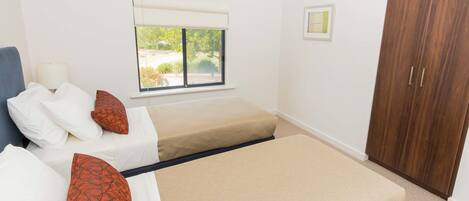 A bedroom with two beds, a window with a view, a wardrobe, and a bedside table.