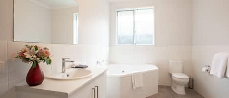 A modern bathroom with a large mirror, a sink, a bathtub, and a toilet.