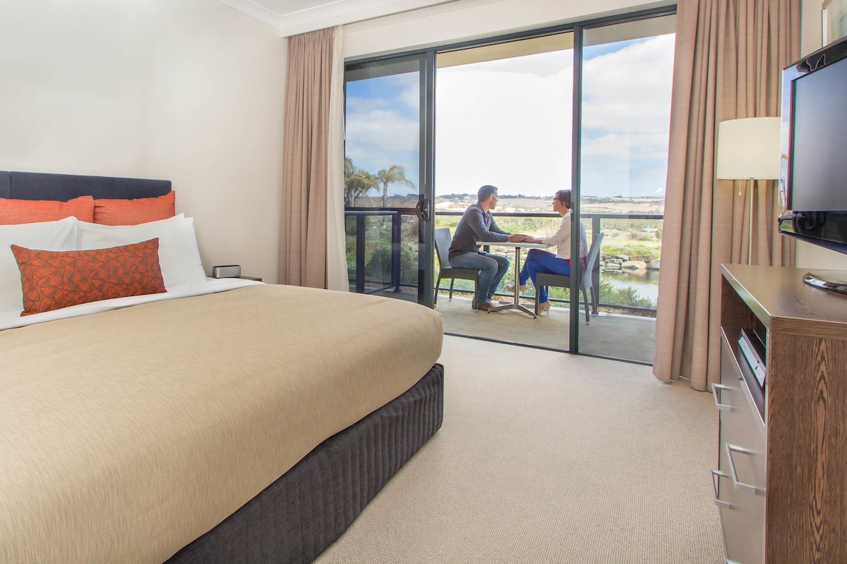 A hotel room with a large bed, a TV, and a balcony with a view.