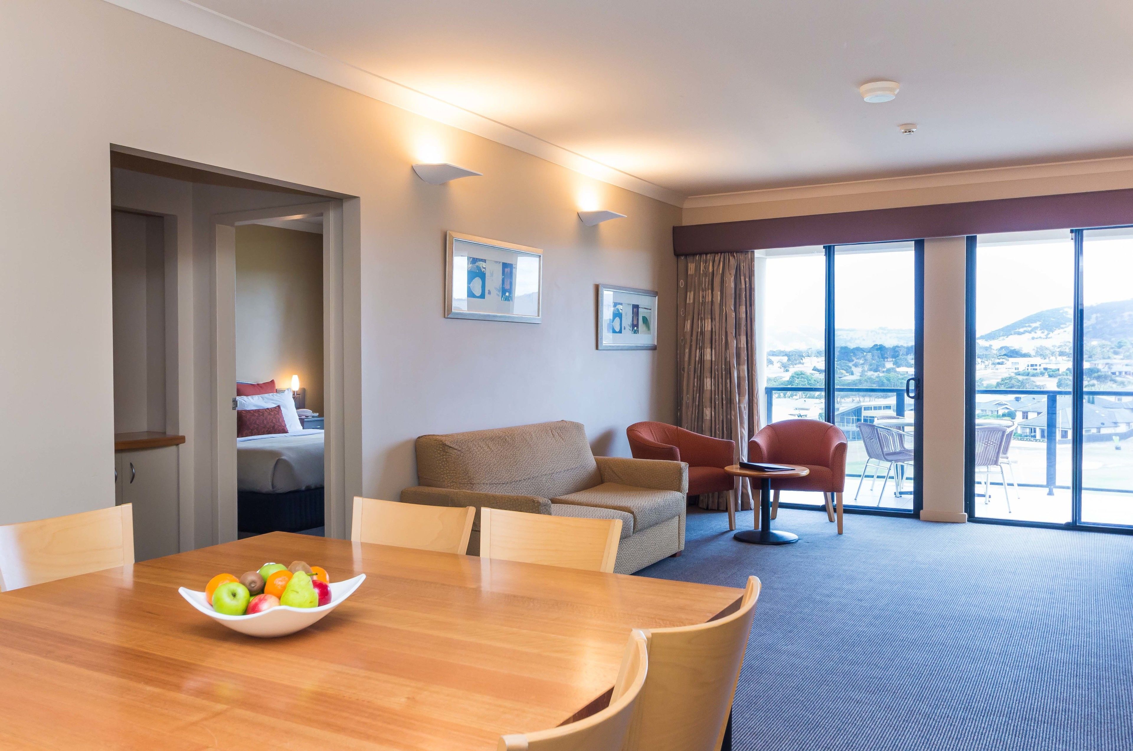Habitación de hotel con una mesa de comedor, un sofá, una silla y un balcón con vistas.