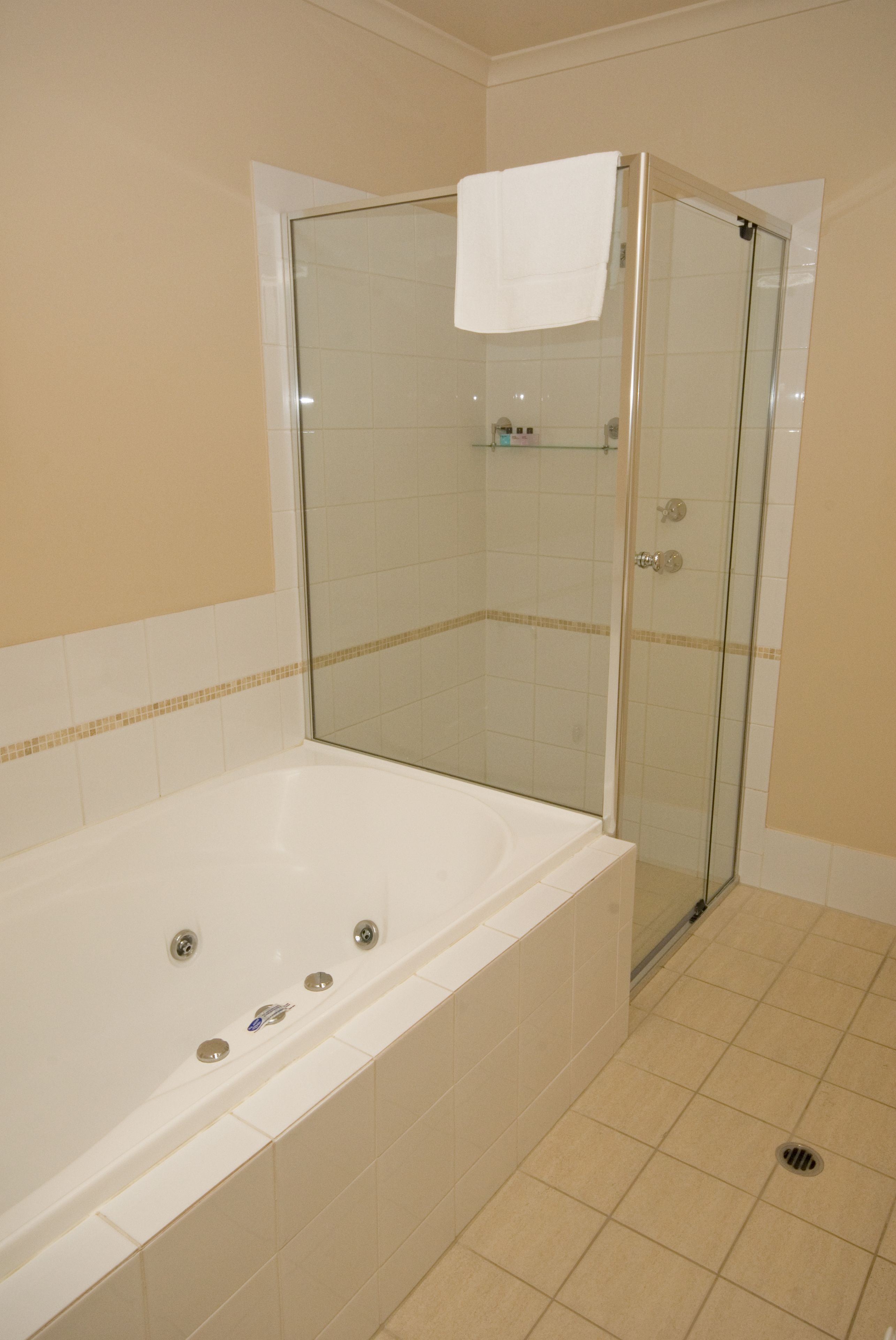 A bathroom with a glass-enclosed shower, a white bathtub, and beige tiled walls.