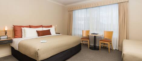 Ein Hotelzimmer mit einem großen Bett, einem Schreibtisch, zwei Stühlen, einem Deckenventilator und einem fenster mit Vorhängen.