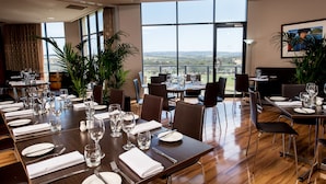 Comedor con mesas dispuestas para una comida, ventanas amplias con vistas y plantas en macetas.