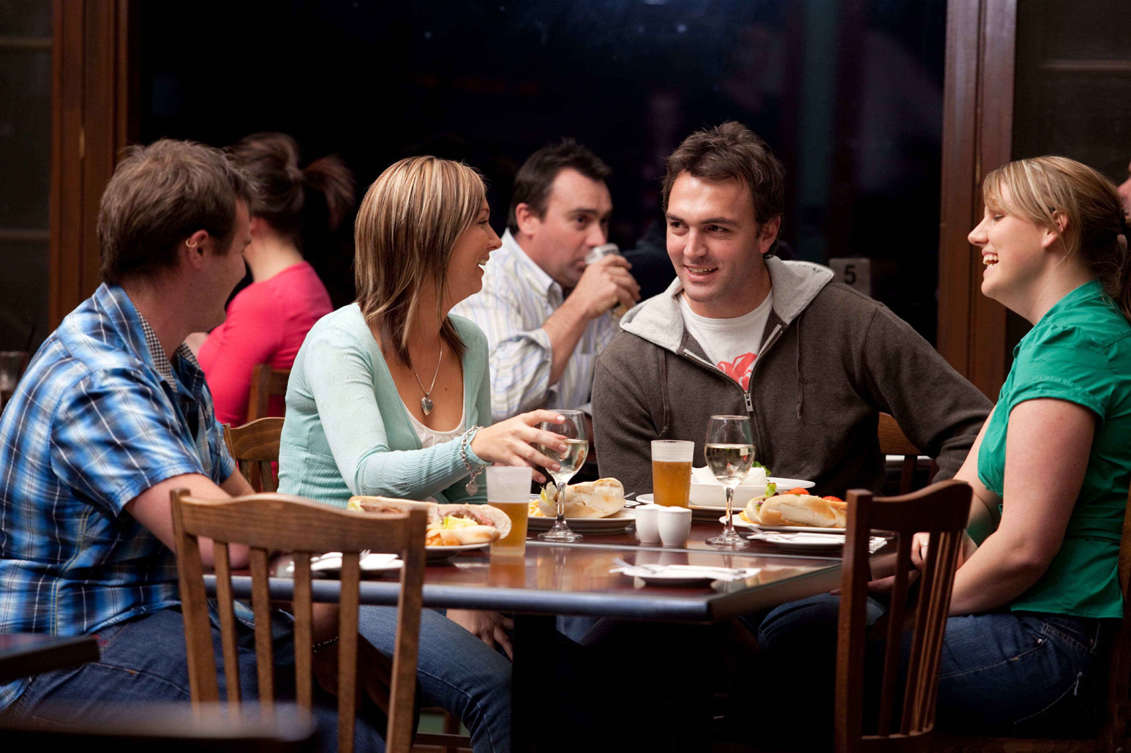 A group of people sitting around a table in a restaurant with wooden chairs and a dark interior.