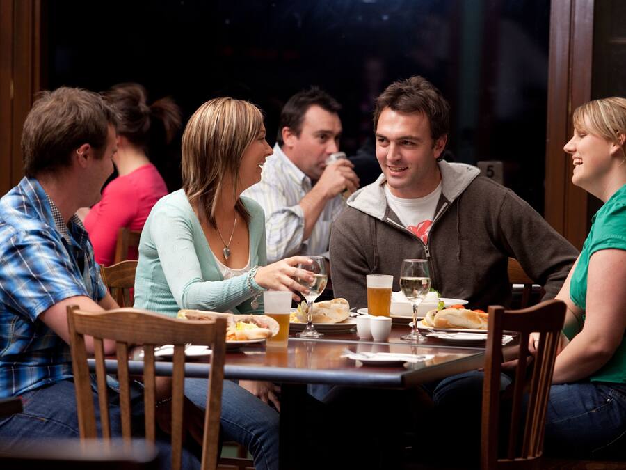 A group of people sitting around a table in a restaurant with wooden chairs and a dark interior.