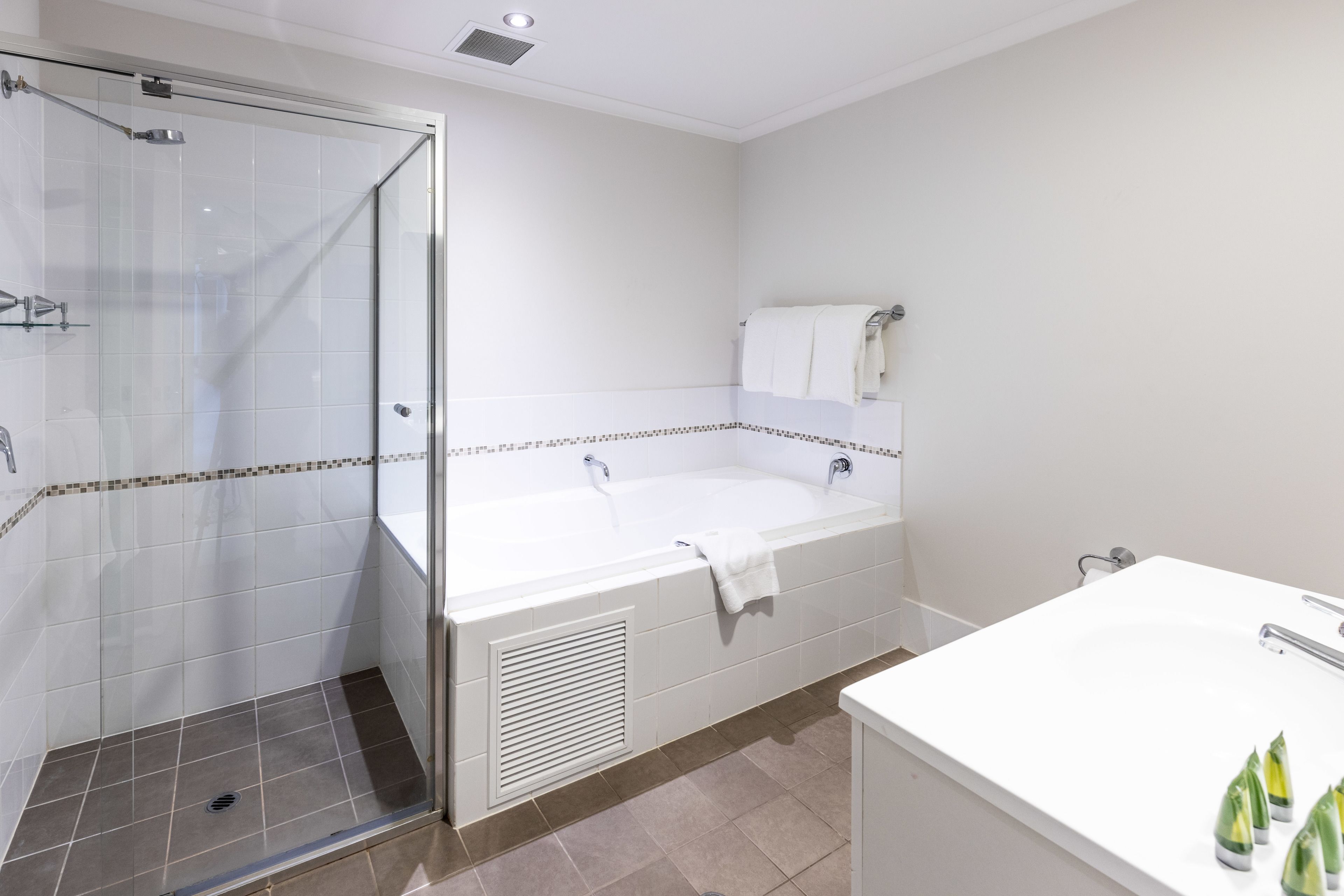 Un baño moderno con ducha de vidrio, una bañera independiente y un lavamanos blanco con artículos de aseo.