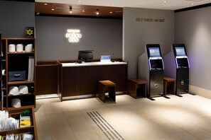A self-service check-in/out area with a reception desk, computer, and self-service kiosks.