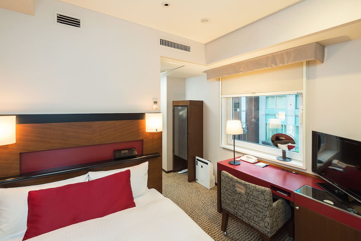 A hotel room with a bed, desk, chair, TV, and window with a view.