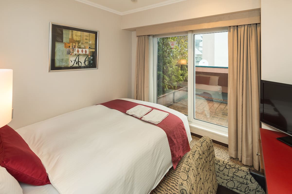 A hotel room with a bed, a television, a window with curtains, and a framed artwork on the wall.