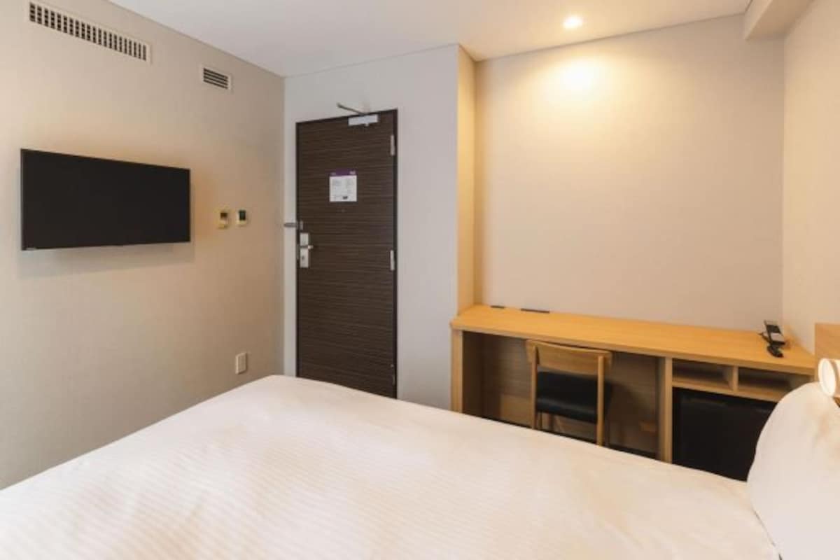 Ett hotellrum med en säng, ett skrivbord, en tv och en dörr.