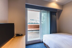 A hotel room with a bed, a television, a desk, and a window with curtains.