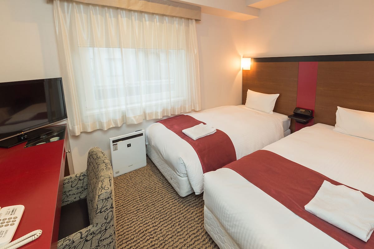 A hotel room with two beds, a TV, a desk, and a small desk fan.