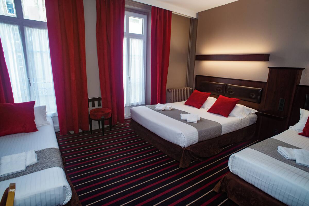 A hotel room with two beds, red curtains, a radiator, and a striped carpet.