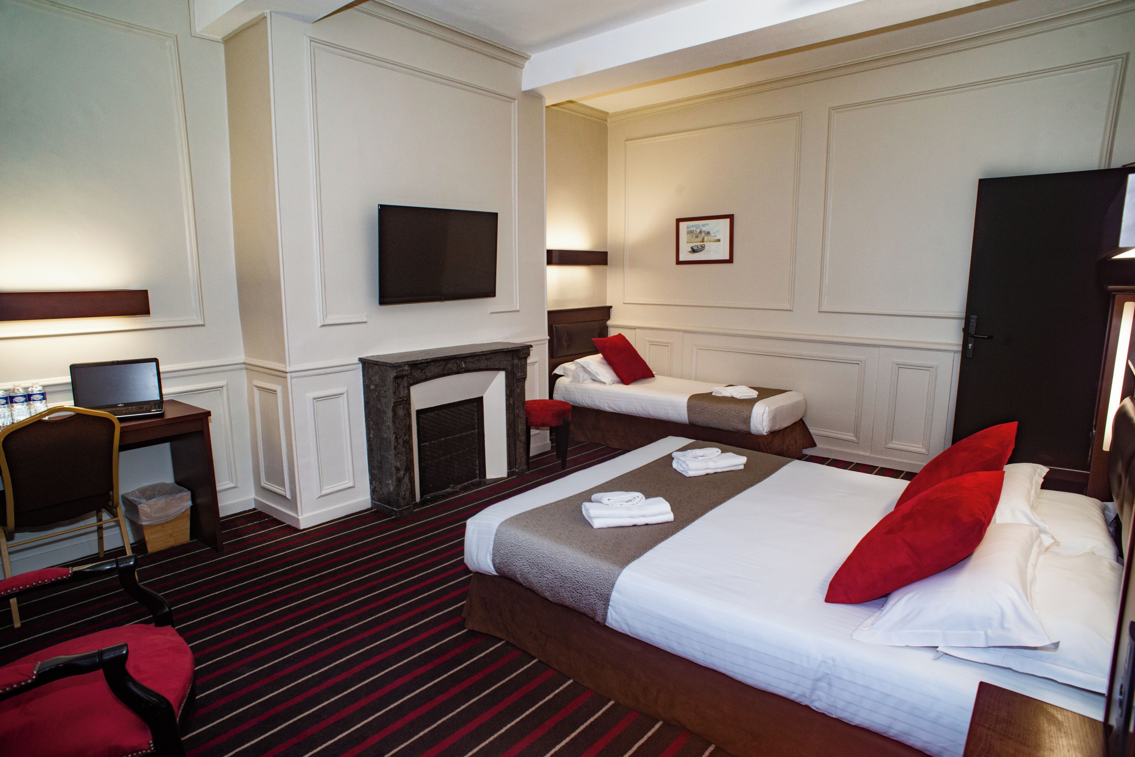 Hotelkamer met een groot bed, een kleiner bed, een bureau met een computer, een stoel en een open haard.
