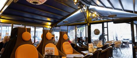 Un restaurante con sillas anaranjadas de respaldo alto, una lámpara de techo con diseño y vistas a la calle.