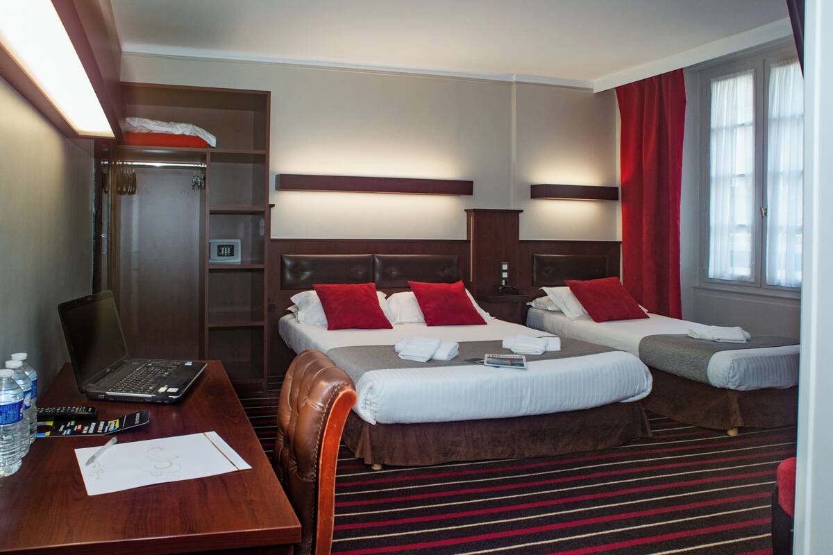 A hotel room with two beds, a desk with a laptop, and a wardrobe.